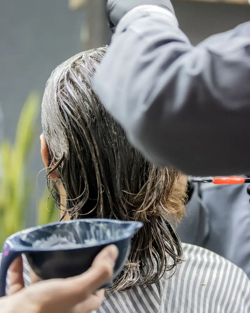Colouristin trägt mit Pinsel und Schale ein Glossing auf langes, nasses Haar auf